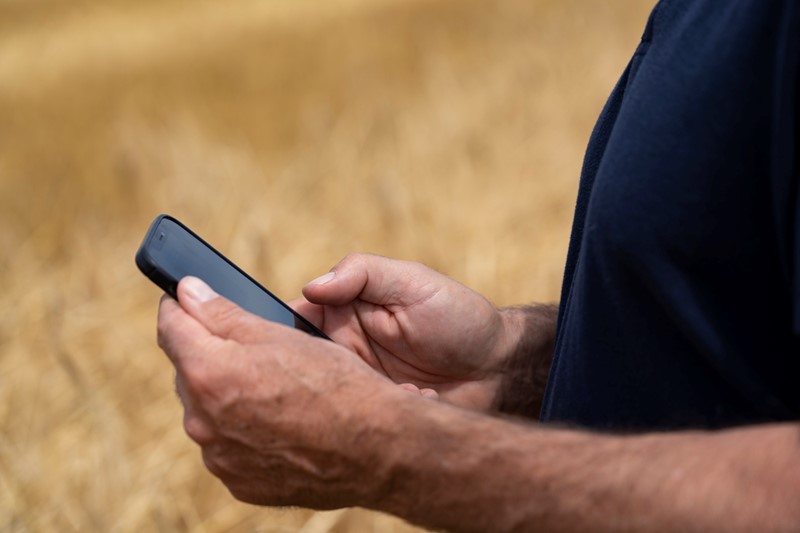 Close up image of a farmer looking at his phone in an arable field.