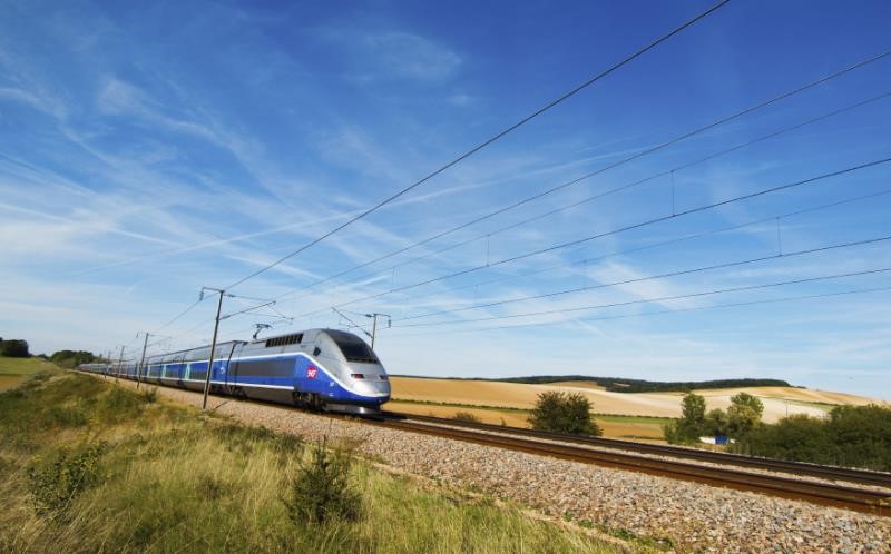 A picture of a high speed train going through the countryside on a sunny day.